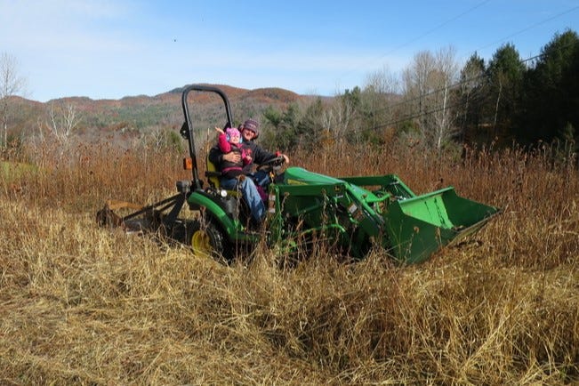 A father and daughter ride their tractor to mow their meadow in fall