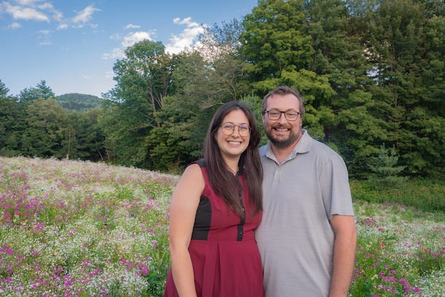 A smiling couple standing together in their colorful wildflower meadow